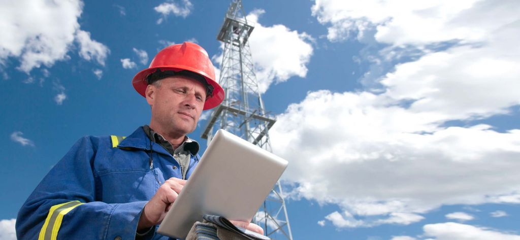 Engineer with tablet and oil rig tower- Locus software solutions for the Energy, Oil & Gas industries